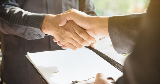 Two hands shaking over binder of paper