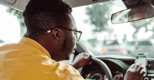 A man typing something into a ridesharing app while he is driving