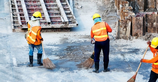 workers on a boat wearing hard hats and reflective vests, sweeping a water-soaked area